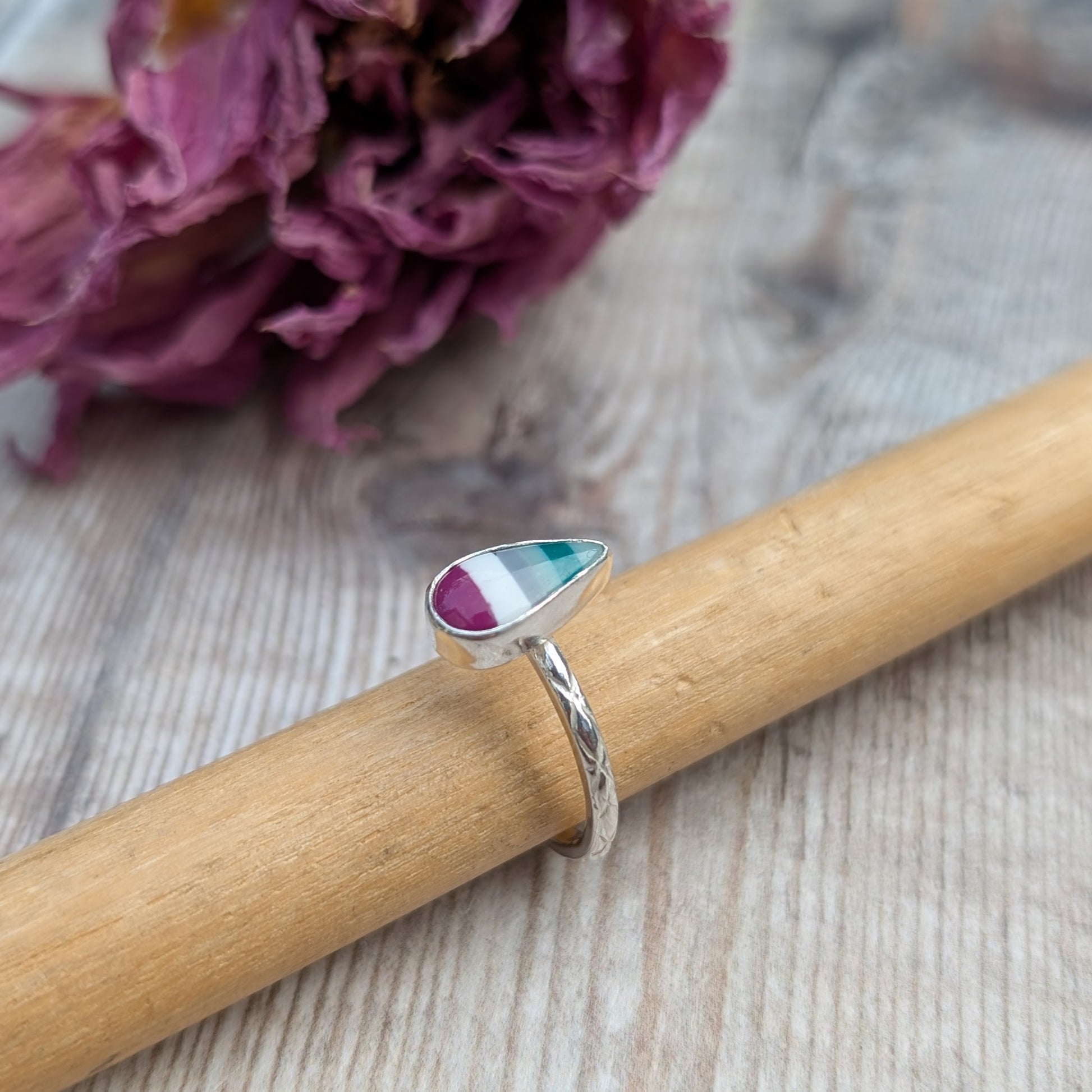Handmade silver Surfite ring with a teardrop stone resting on a wooden ring mandrel, showing engraved band detail.