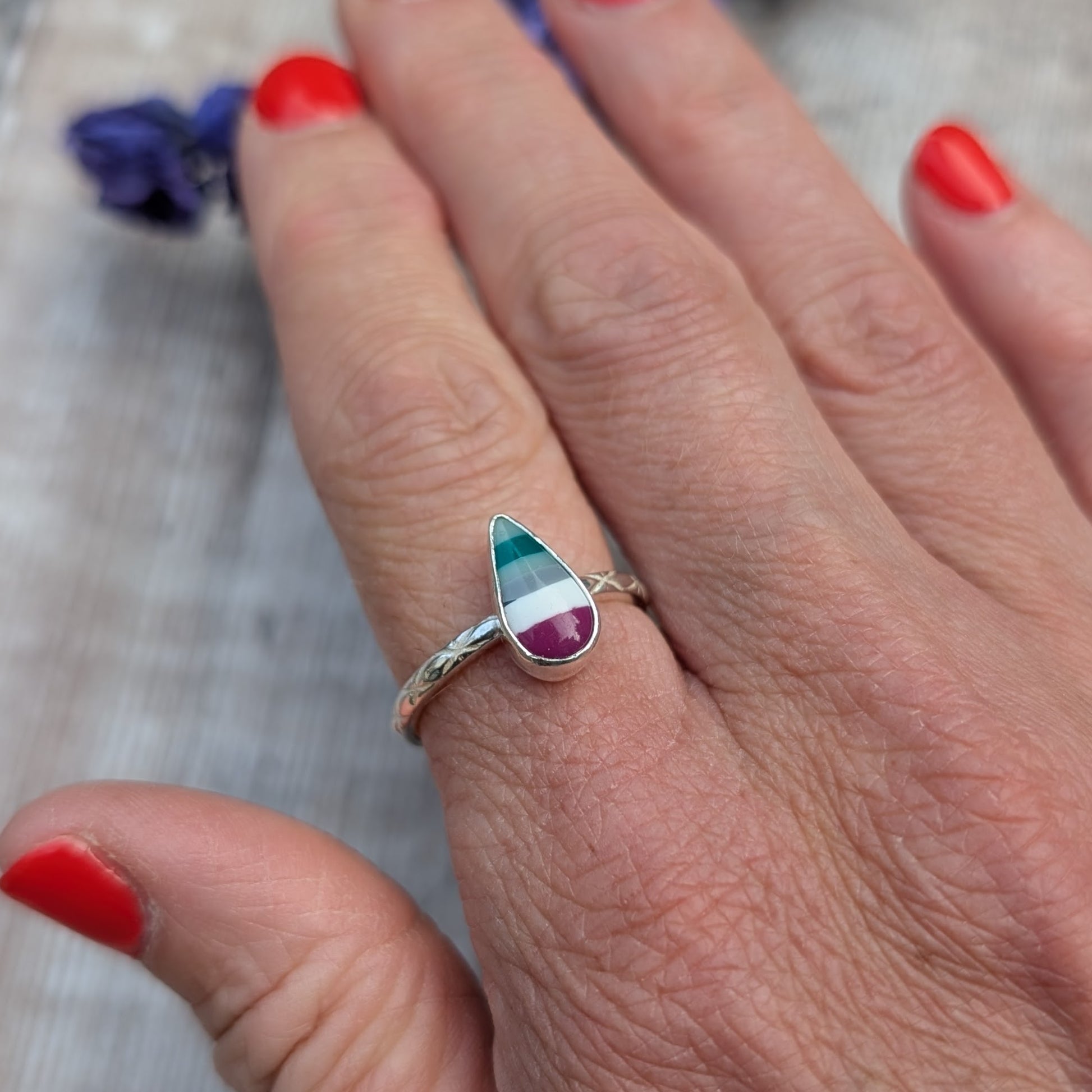 Surfite teardrop ring worn on a hand, displaying the rich colours of the stone and the pattern on the silver band.