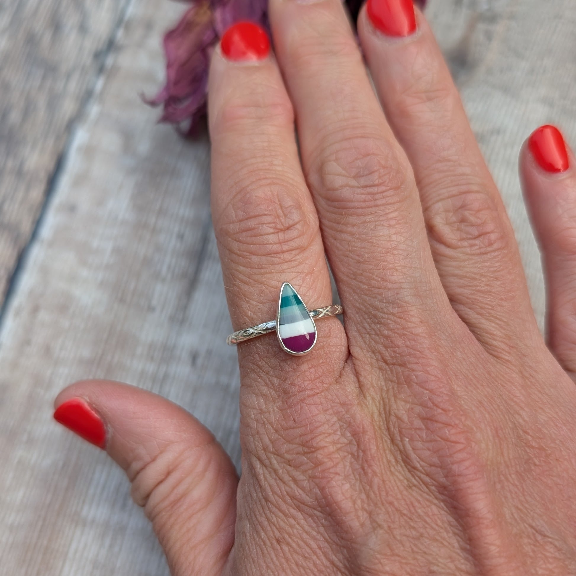 Surfite teardrop ring worn on a hand, displaying the rich colours of the stone and the pattern on the silver band.