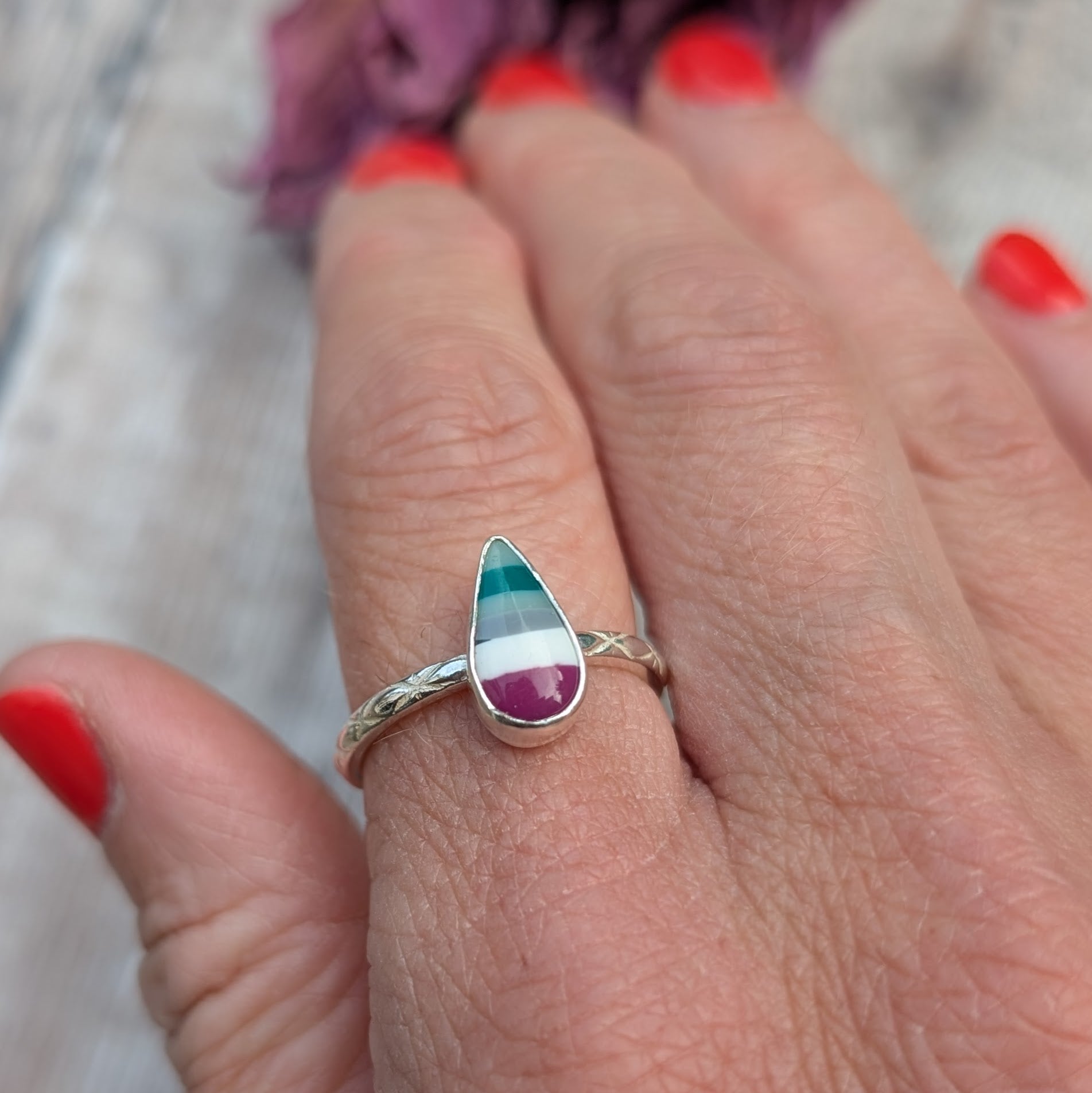 Surfite teardrop ring worn on a hand, displaying the rich colours of the stone and the pattern on the silver band.