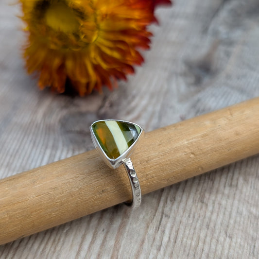 Close-up of a handmade silver ring with a triangle-shaped Surfite stone, resting on a wooden ring mandrel.