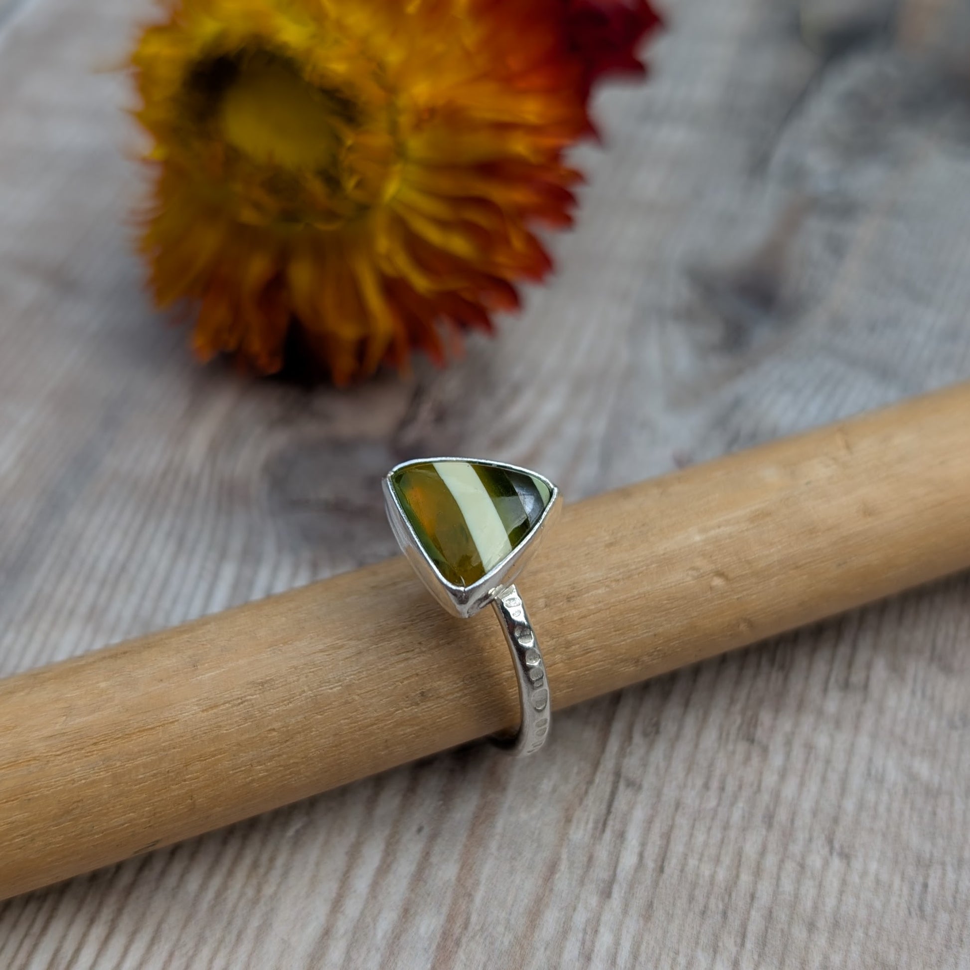 Close-up of a handmade silver ring with a triangle-shaped Surfite stone, resting on a wooden ring mandrel.