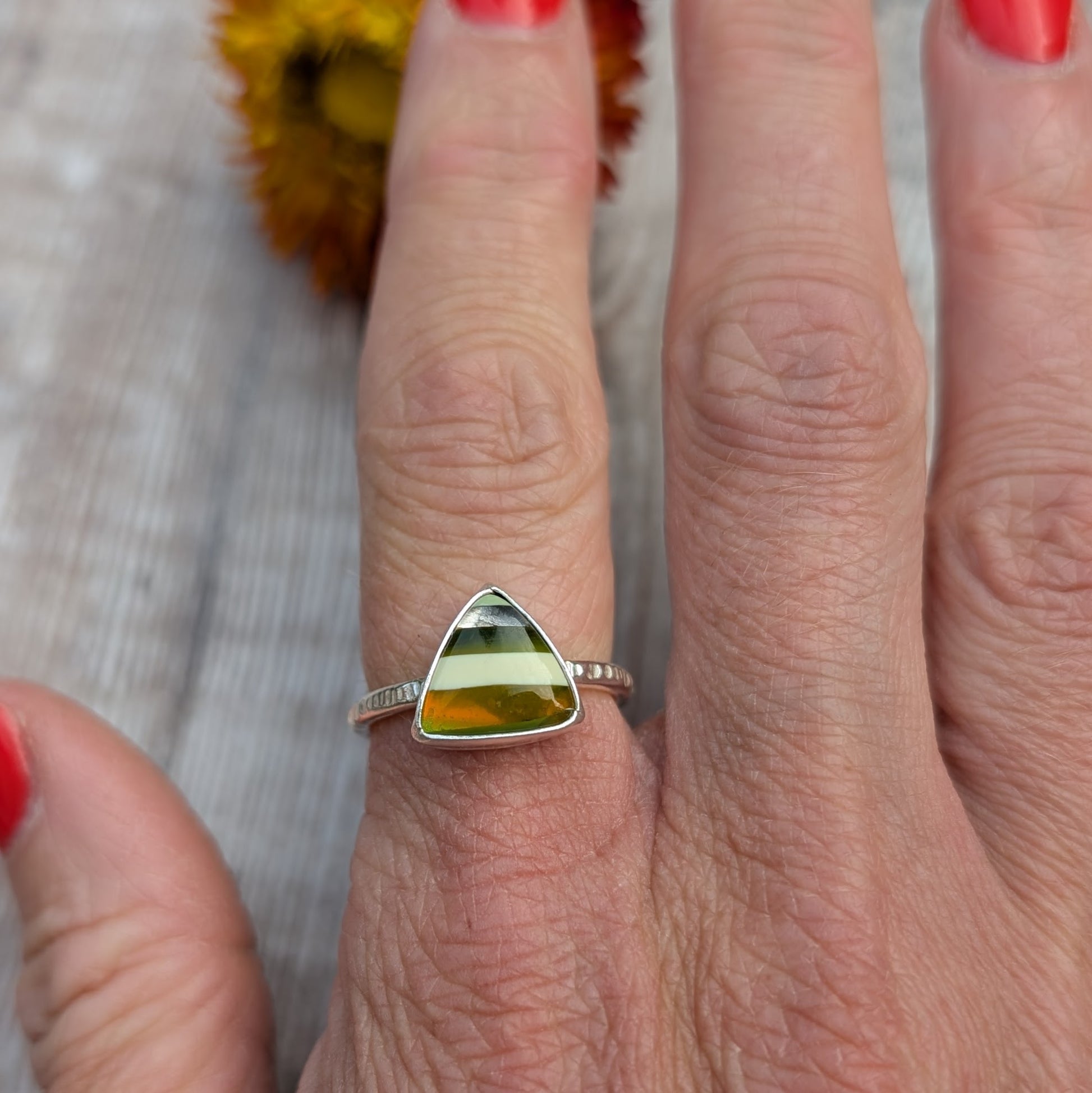 Hand wearing a silver ring with a striped Surfite triangle stone in green, white, and amber tones.