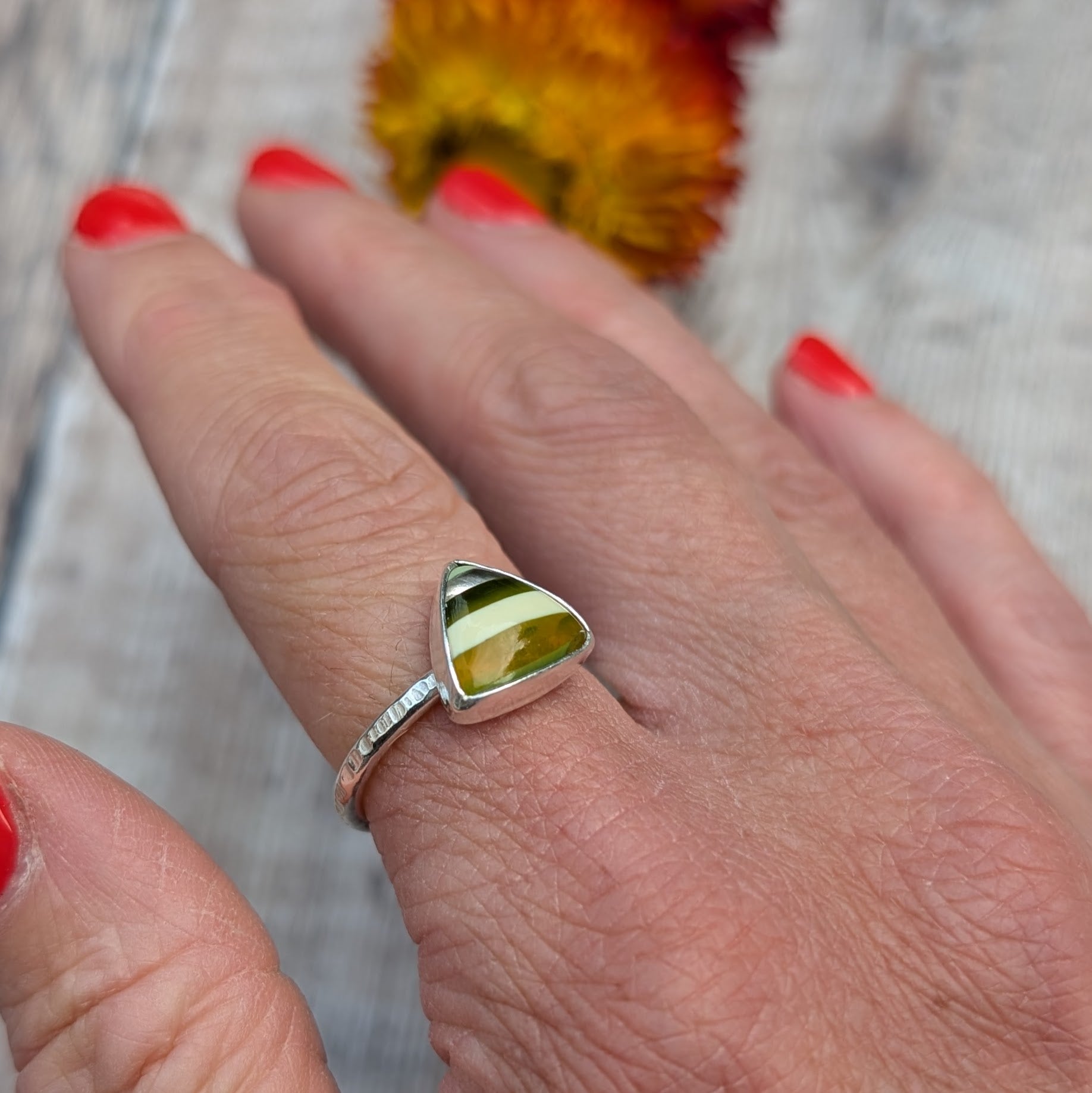 Hand wearing a silver ring with a striped Surfite triangle stone in green, white, and amber tones.