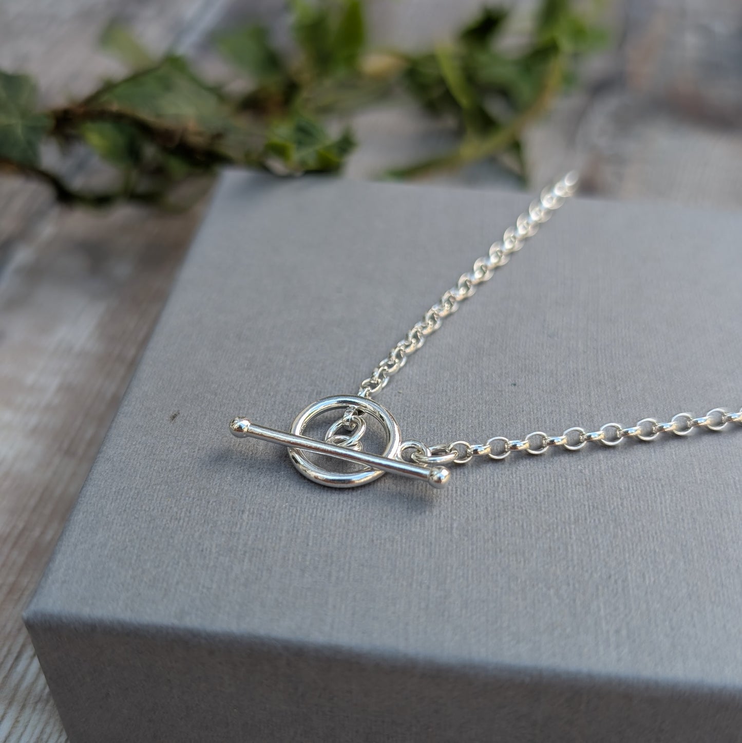 Close-up of a Silver T Bar Necklace handmade from recycled Sterling Silver, featuring a sterling silver chain and polished T bar clasp on a grey jewellery box.