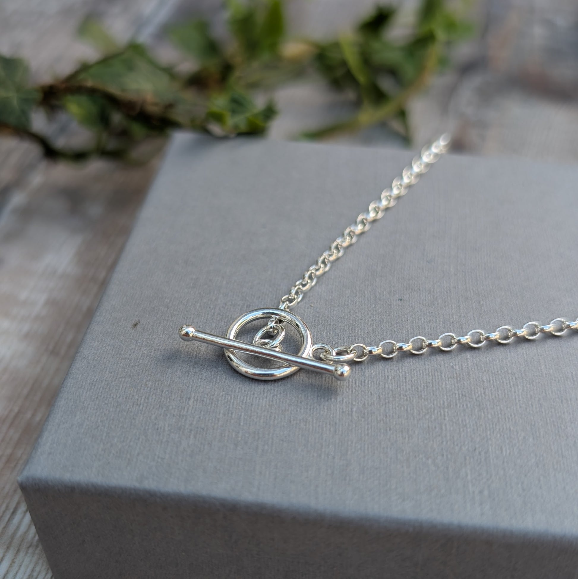 Close-up of a Silver T Bar Necklace handmade from recycled Sterling Silver, featuring a sterling silver chain and polished T bar clasp on a grey jewellery box.