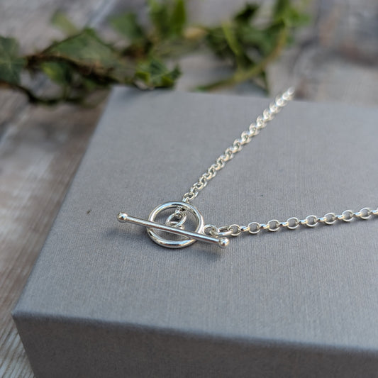 Close-up of a Silver T Bar Necklace handmade from recycled Sterling Silver, featuring a sterling silver chain and polished T bar clasp on a grey jewellery box.