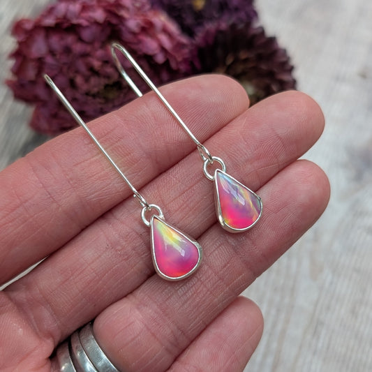 Close-up view of a hand holding a pair of Silver Teardrop Earrings with Pink Aurora Opal, showing their iridescent colours ranging from pink to yellow and hints of blue.