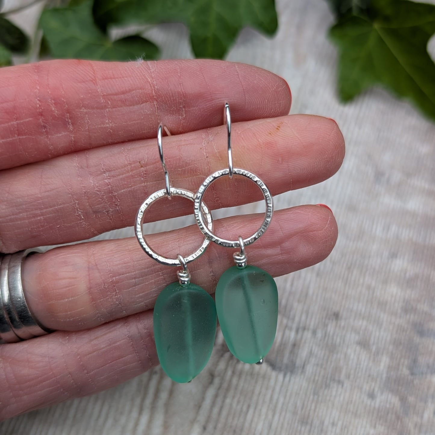 Close-up of handmade Silver Textured Circle Earrings with Aqua Sea Glass Beads held in a hand to show size and detail.
