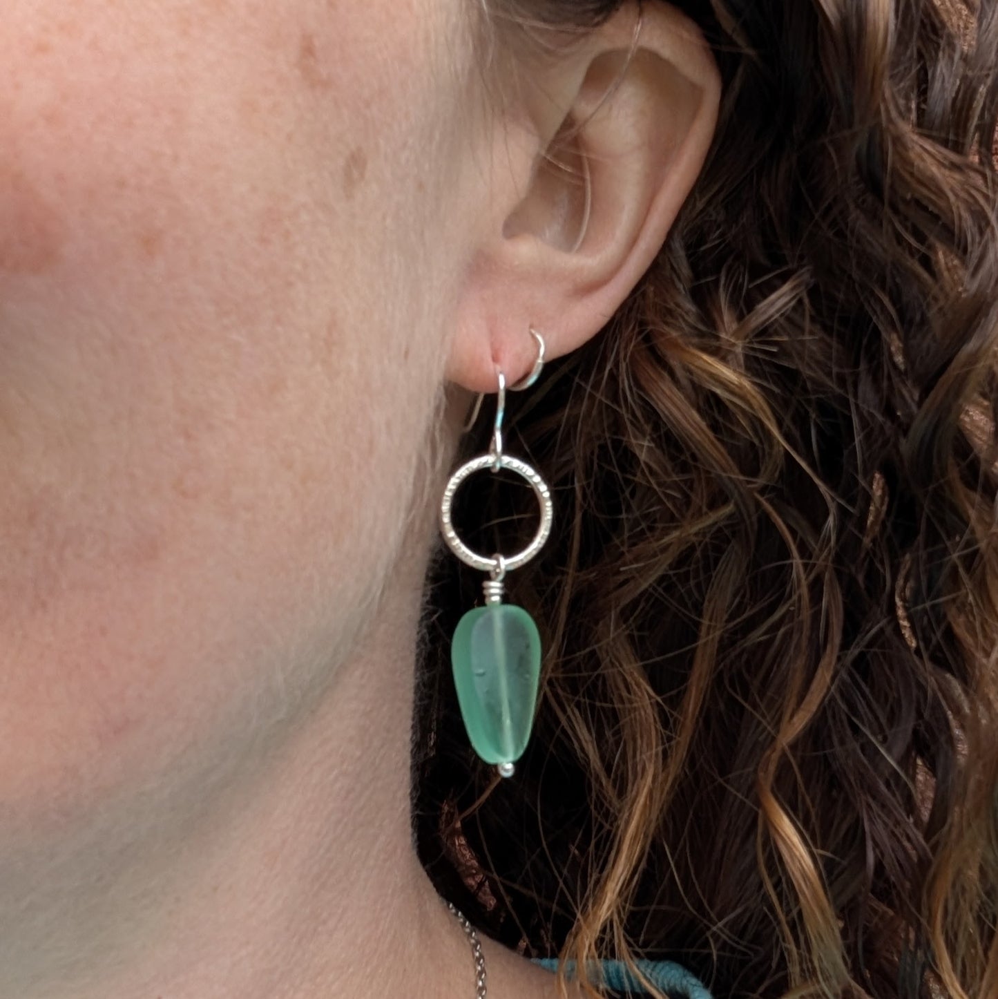 Silver Textured Circle Earrings with Aqua Sea Glass Beads being worn in the ear.
