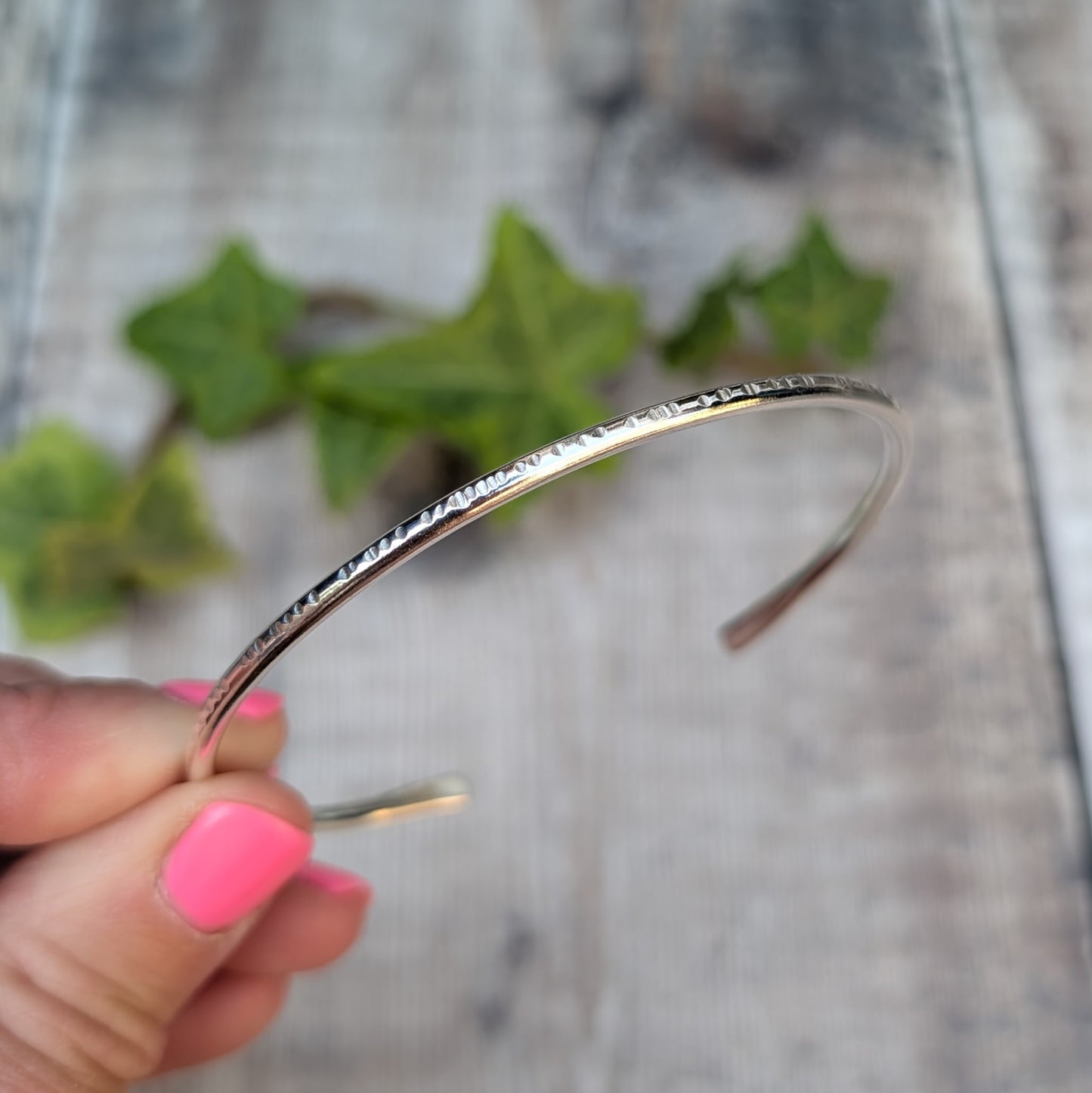 Silver Textured Oval Cuff Bangle held in hand, with a close up view of the hammered edge texture and open cuff design.