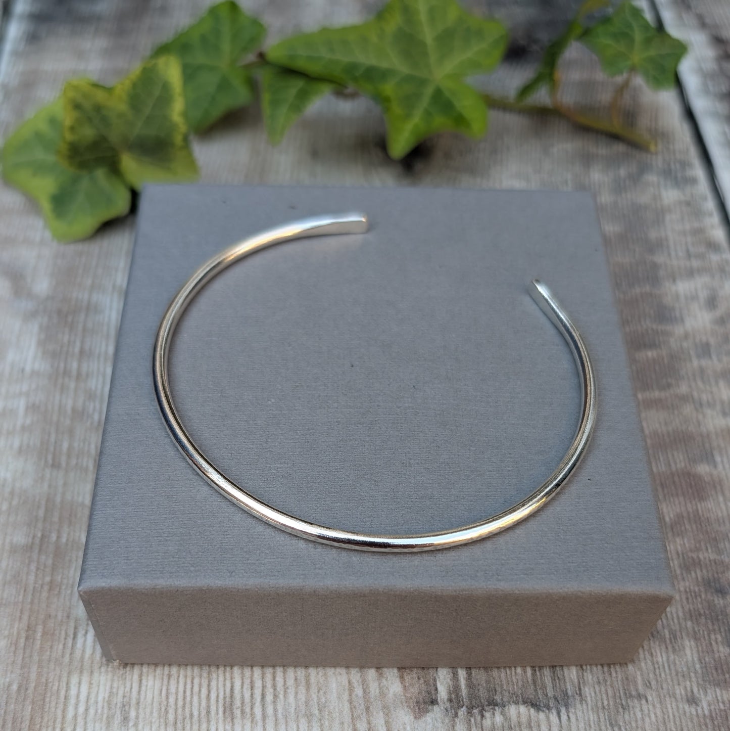 Silver Textured Oval Cuff Bangle displayed on a grey jewellery box, showing the open oval cuff shape.