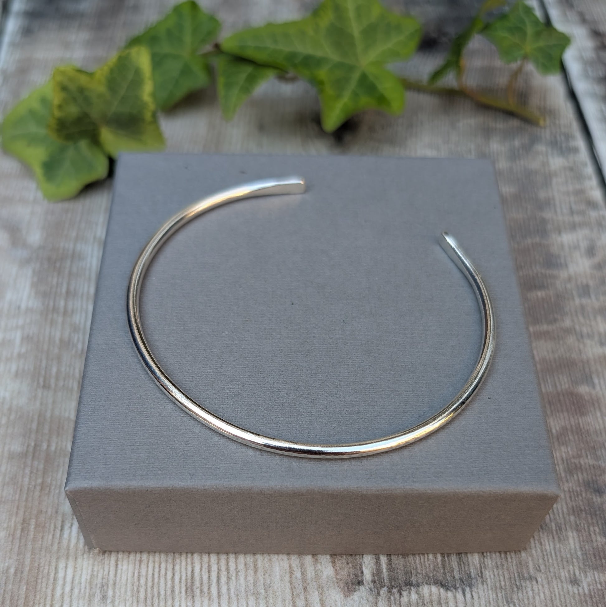 Silver Textured Oval Cuff Bangle displayed on a grey jewellery box, showing the open oval cuff shape.