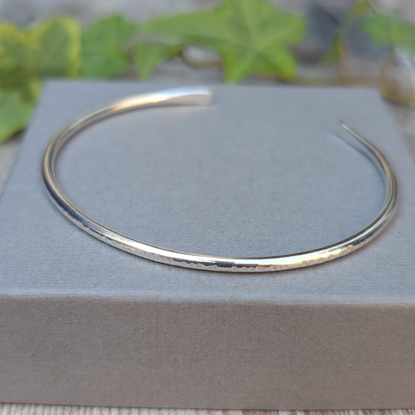 Close up of Silver Textured Oval Cuff Bangle on a grey jewellery box, showing the hammered texture along the edge of the recycled Sterling Silver.