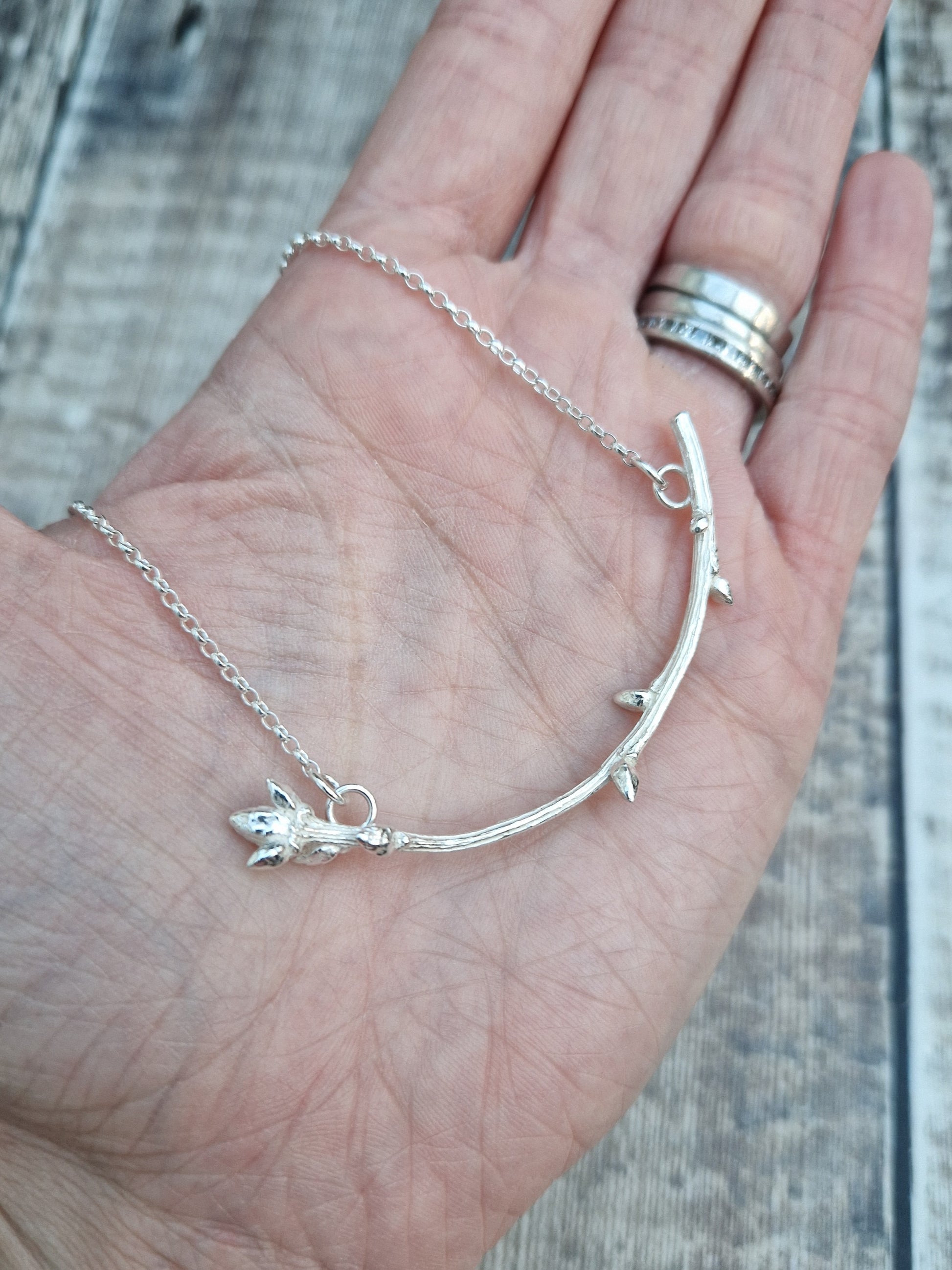 Pendant is a Sterling Silver twig/branch in bud along the stem and a larger bud at the end, curved in shape, attached to silver chain via two small circle links at each end of the branch.