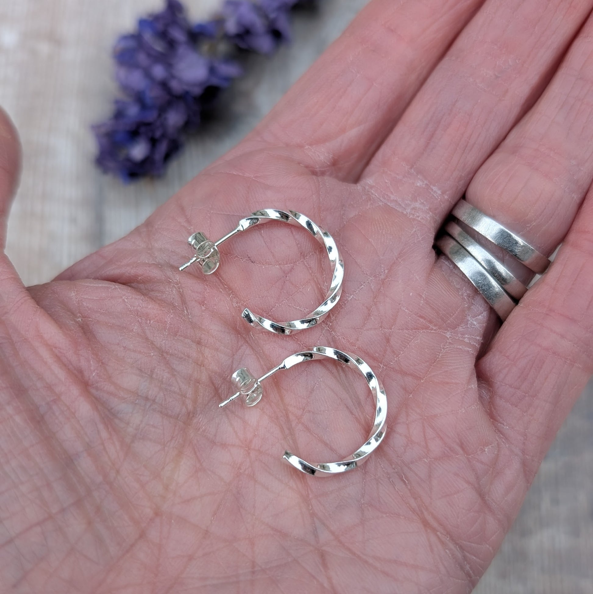 Hand holding a pair of small twisted sterling silver hoop earrings, showing their size and polished finish.