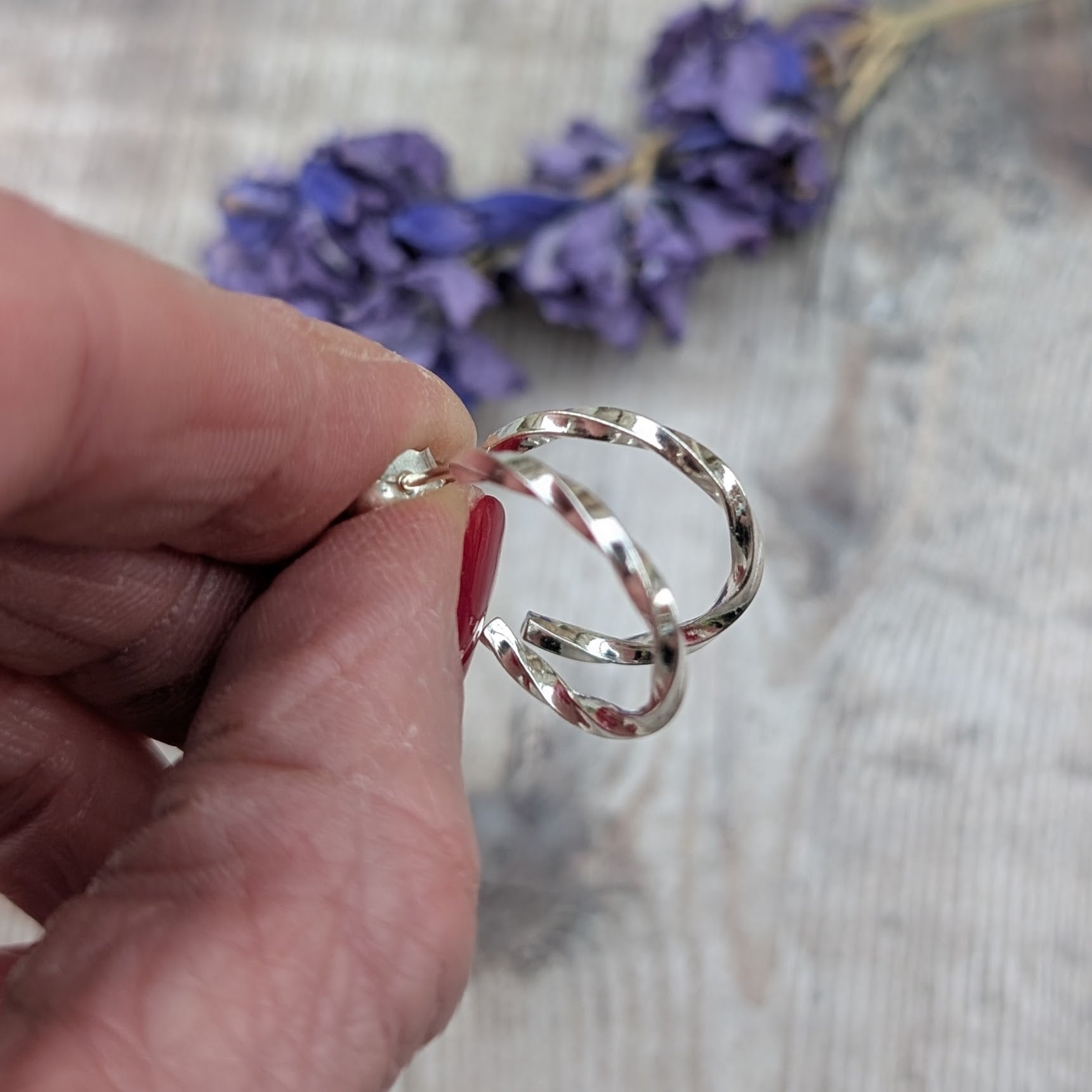 Close-up of twisted sterling silver hoop earrings held between fingers, showing the hammered twist detail and shiny finish.