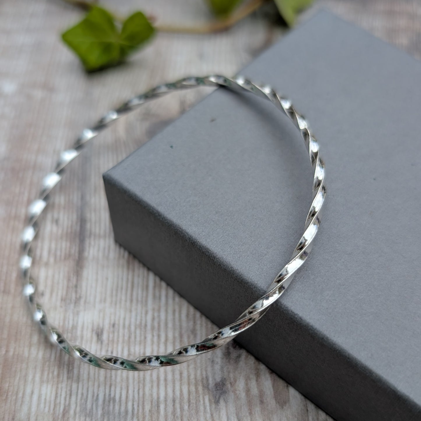 Silver Twisted Round Bangle handmade from recycled Sterling Silver 2mm square wire, photographed at an angle to show the twisted design.