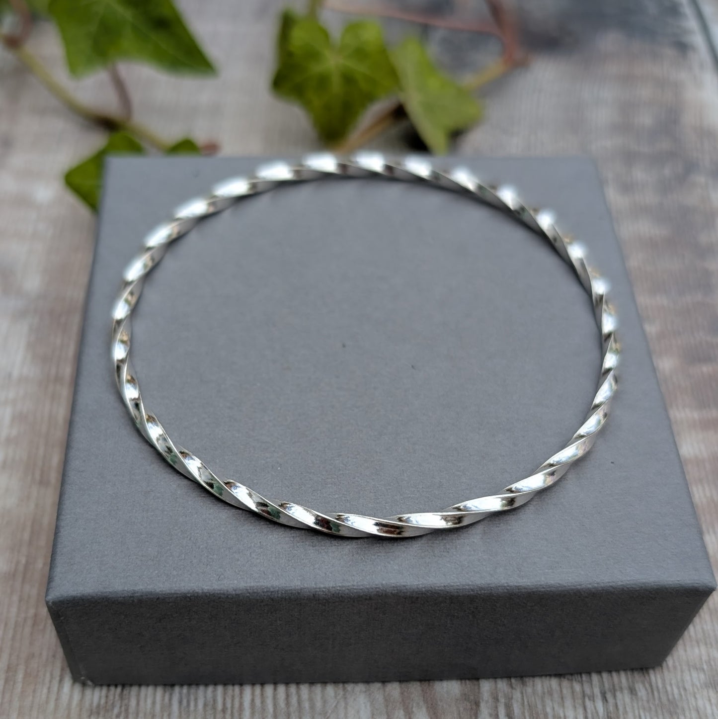 Silver Twisted Round Bangle handmade from recycled Sterling Silver 2mm square wire, shown from above on a grey jewellery box.