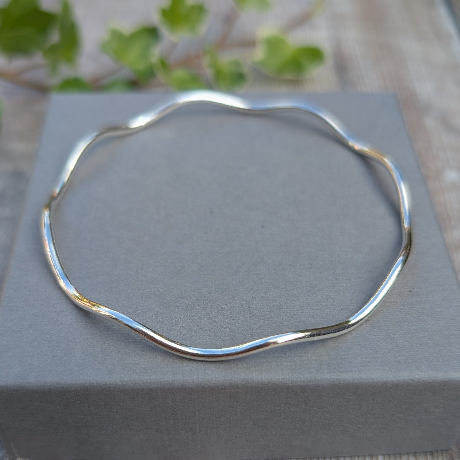 Silver Wavy Round Bangle handmade from recycled Sterling Silver resting on a grey jewellery box, showing the full organic wavy shape.