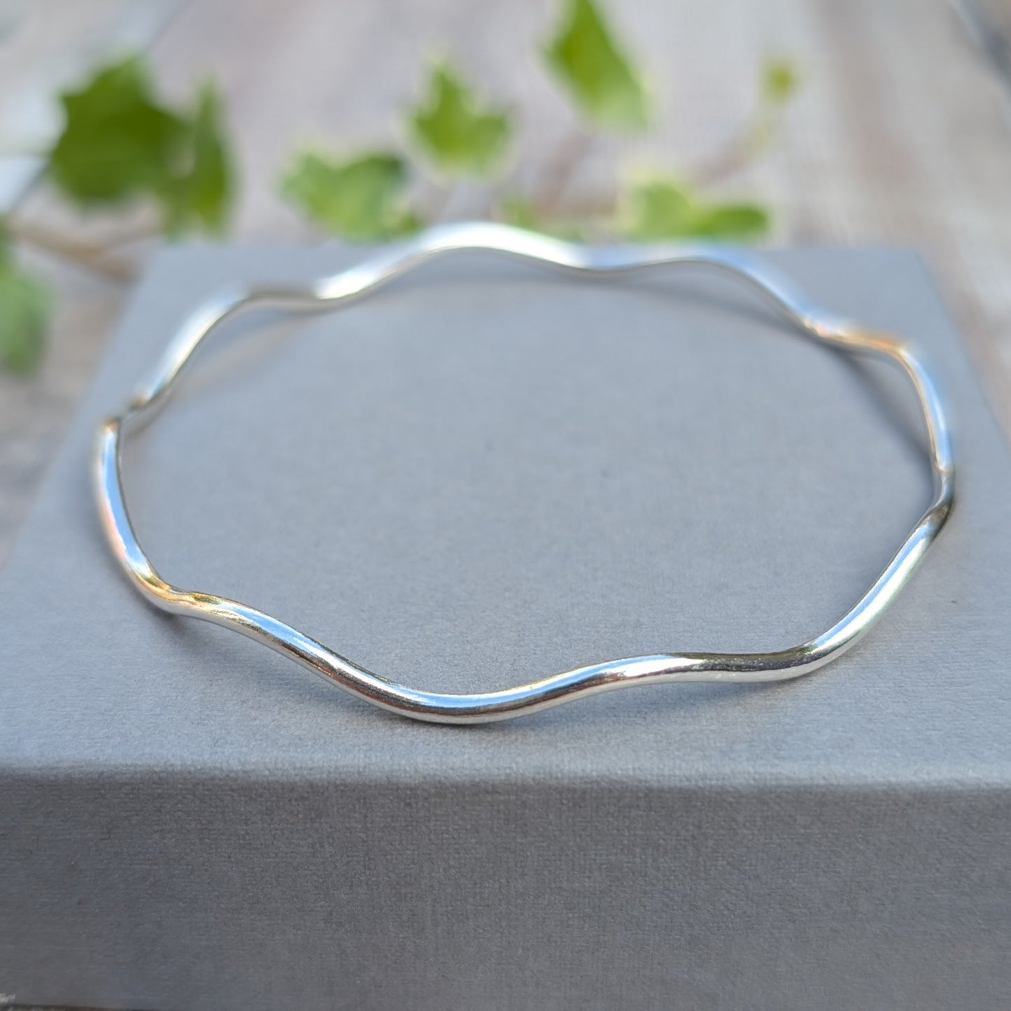 Silver Wavy Round Bangle handmade from recycled Sterling Silver displayed on a grey jewellery box from a low angle, showing the smooth flowing curves.