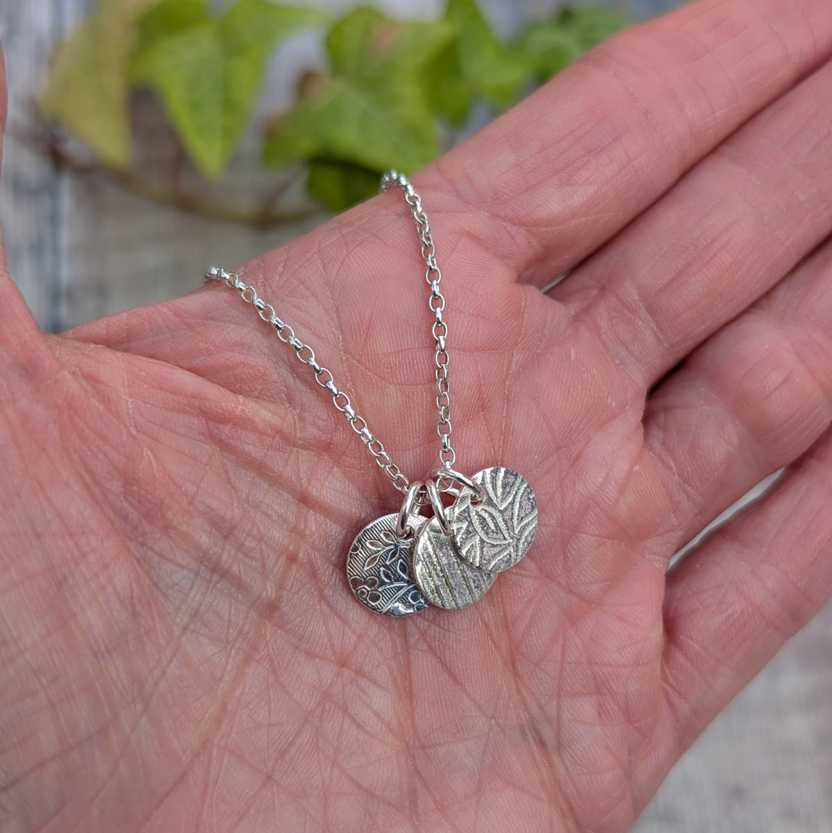 Silver wildflower trio of discs necklace handmade from recycled Sterling Silver, shown resting in a hand with three different patterned silver discs.