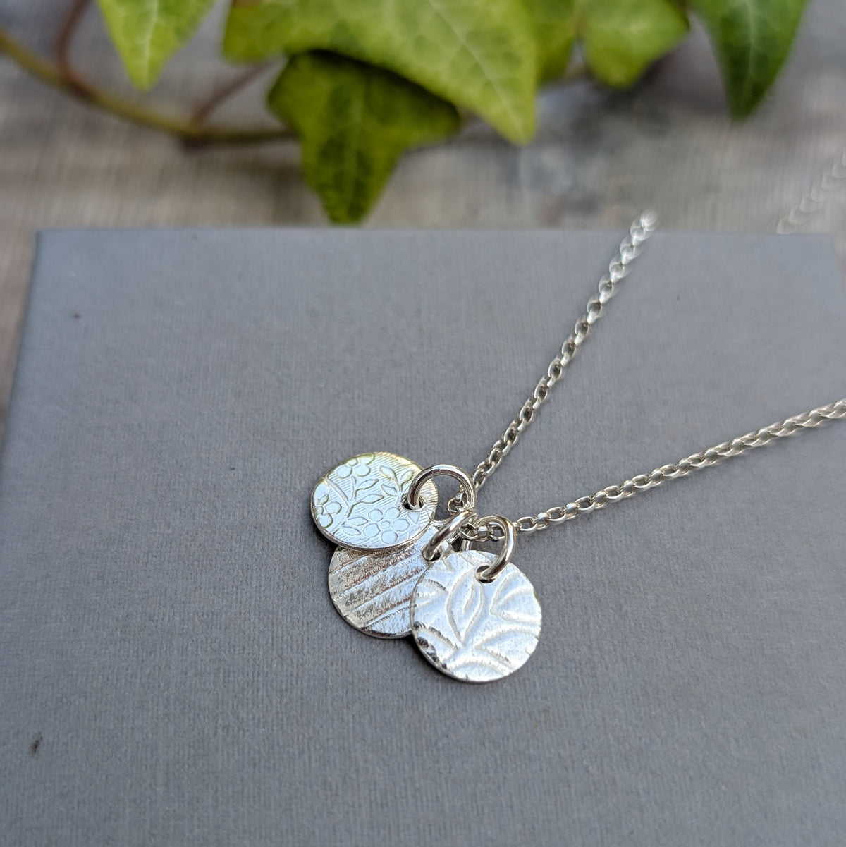 Close up of silver wildflower trio of discs necklace showing the different wildflower and nature inspired patterns applied using a rolling mill.