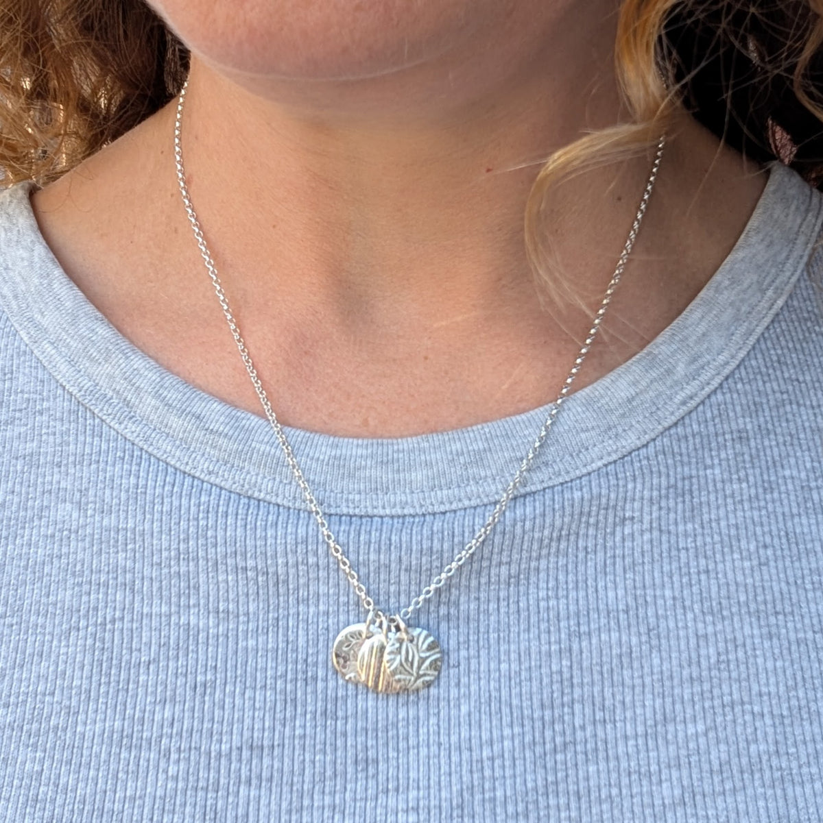 Silver wildflower trio of discs necklace being worn, showing the size and length of the three patterned silver disc pendant.