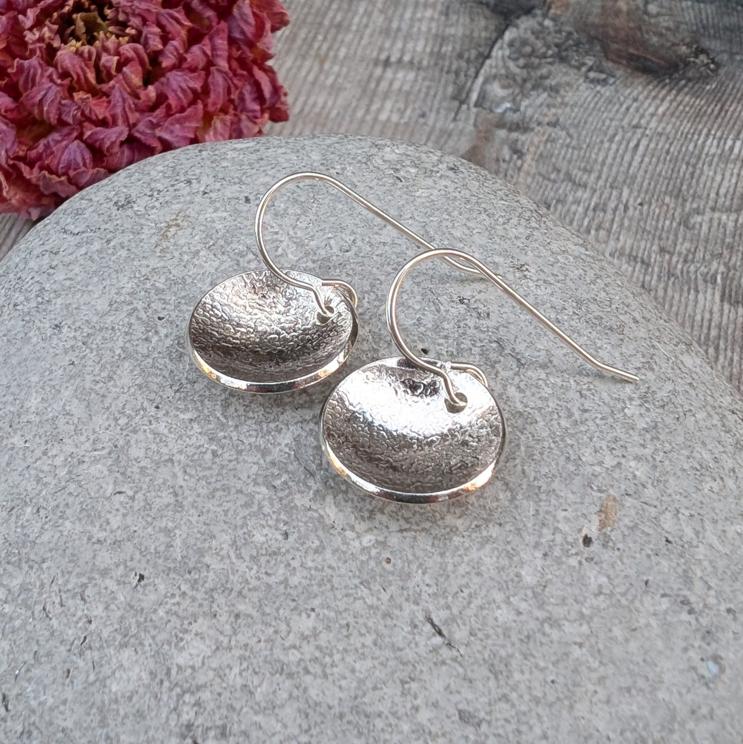 Silver Textured Dome Disc Earrings displayed on a stone surface, highlighting the hammered texture and ear wires