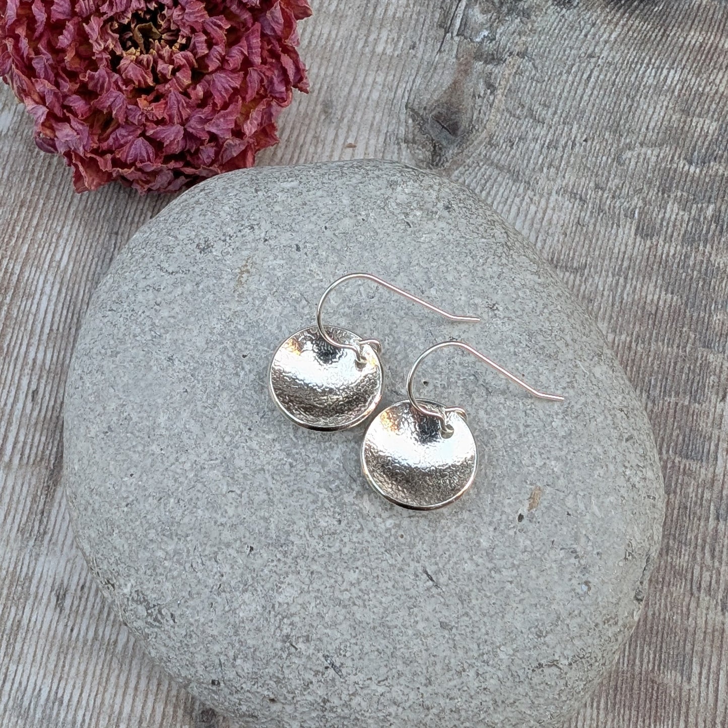 Silver Textured Dome Disc Earrings resting on a smooth stone with a dried flower in the background