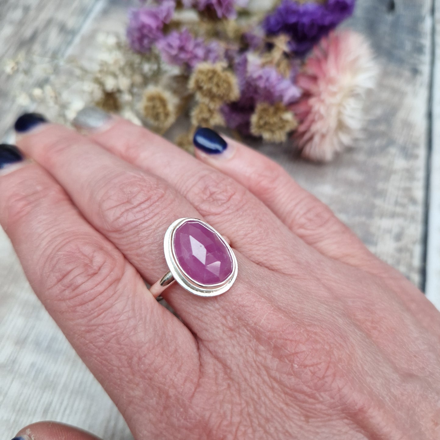 Red Sapphire oval gemstone UK Size R, with diamond cut texture, set in simple silver bezel mounted on top of Sterling Silver band approx. 2mm wide. Sapphire stone is a cloudy mauve colour.