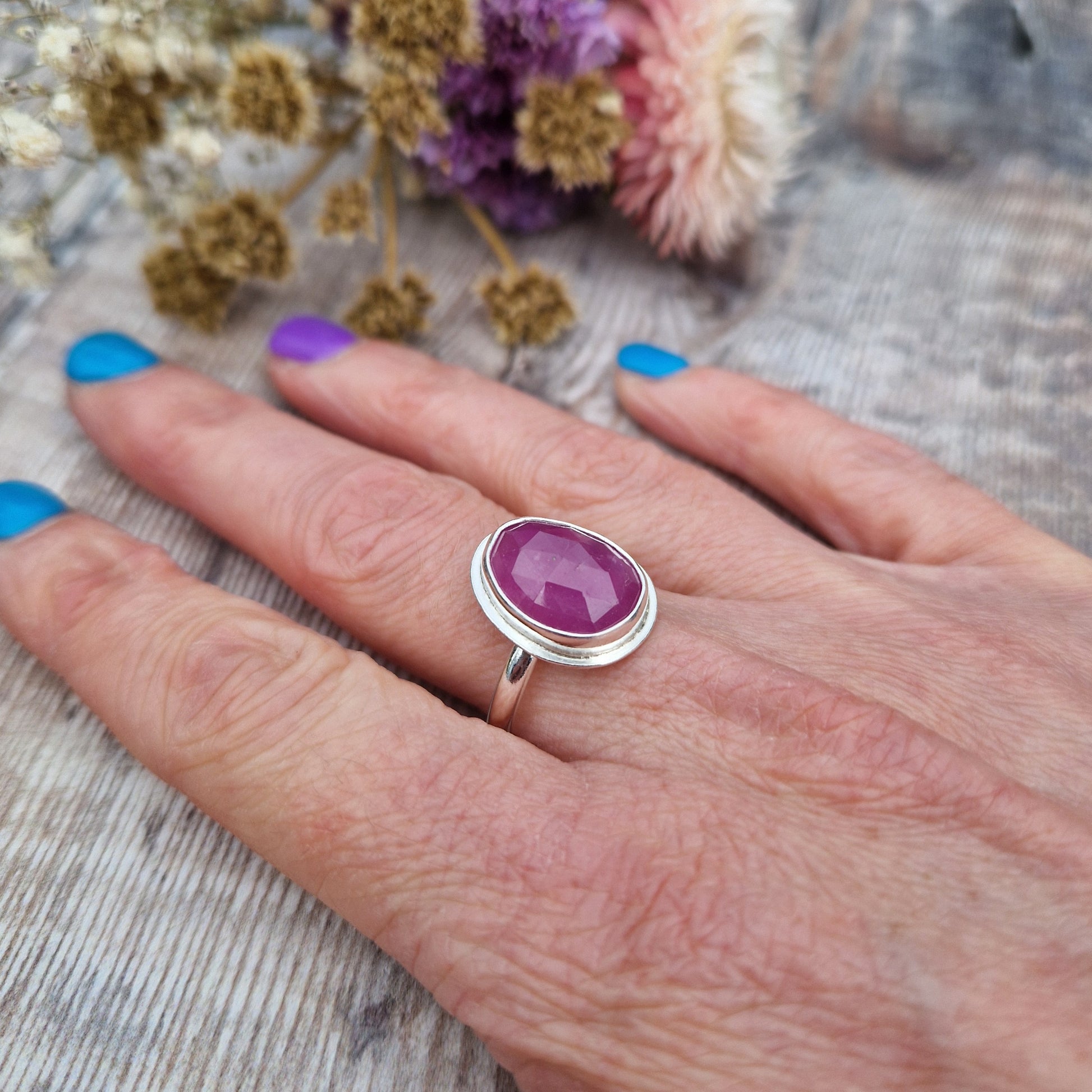 Red Sapphire oval gemstone UK Size R, with diamond cut texture, set in simple silver bezel mounted on top of Sterling Silver band approx. 2mm wide. Sapphire stone is a cloudy mauve colour.