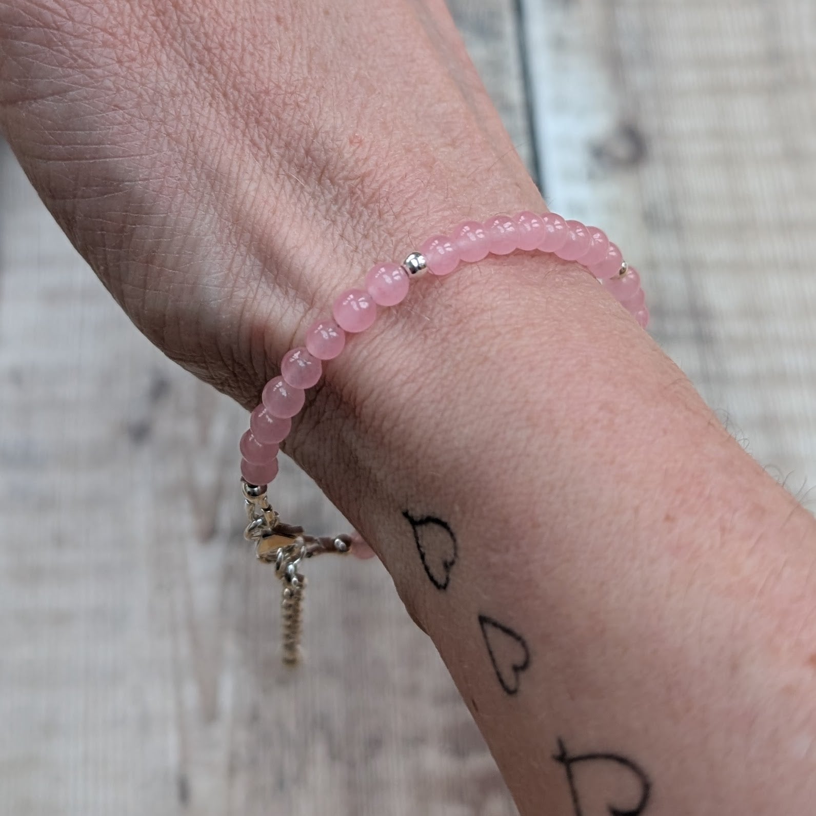 Close-up of a rose quartz bead bracelet worn on the wrist, highlighting the smooth polished beads and silver spacer bead.