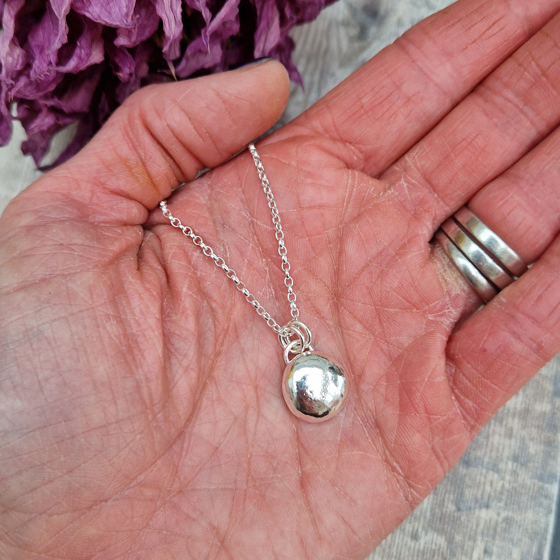 Sterling Silver round pebble shaped pendant with hammered texture, suspended from silver chain via two small circle links.