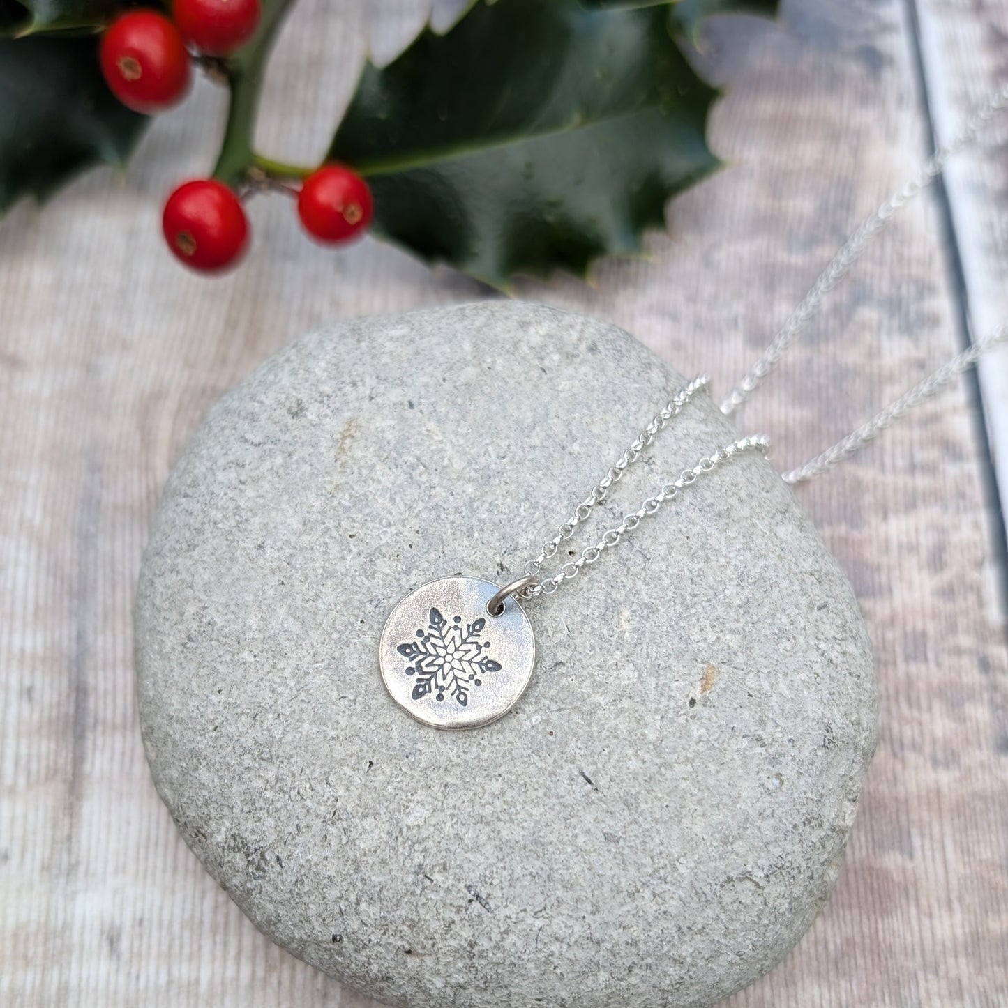 Silver disc pendant necklace featuring a single engraved snowflake design hand stamped onto the disc. Suspended from an 18 inch silver chain via a small open circle link.