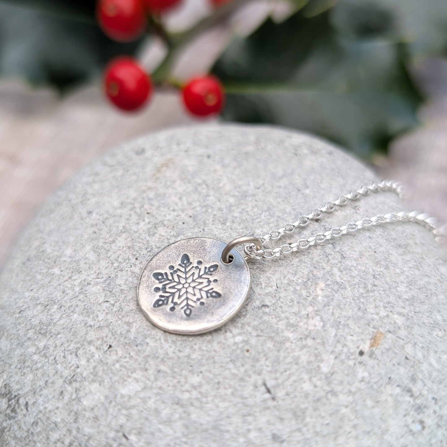 Silver disc pendant necklace featuring a single engraved snowflake design hand stamped onto the disc. Suspended from an 18 inch silver chain via a small open circle link.