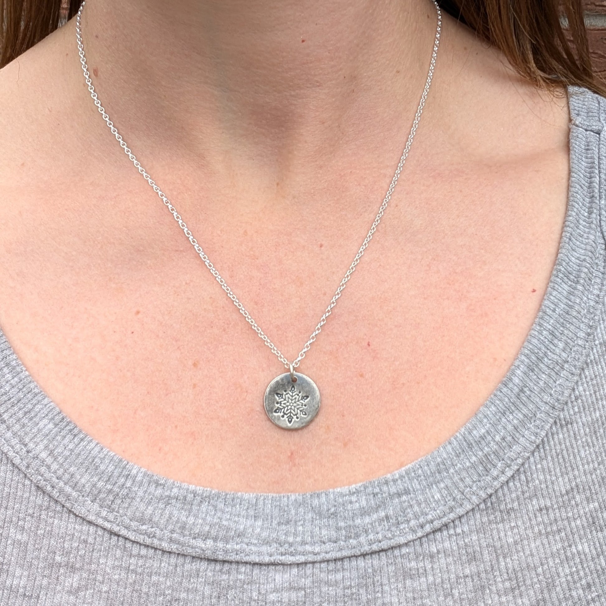 Silver disc pendant necklace featuring a single engraved snowflake design hand stamped onto the disc. Suspended from an 18 inch silver chain via a small open circle link.