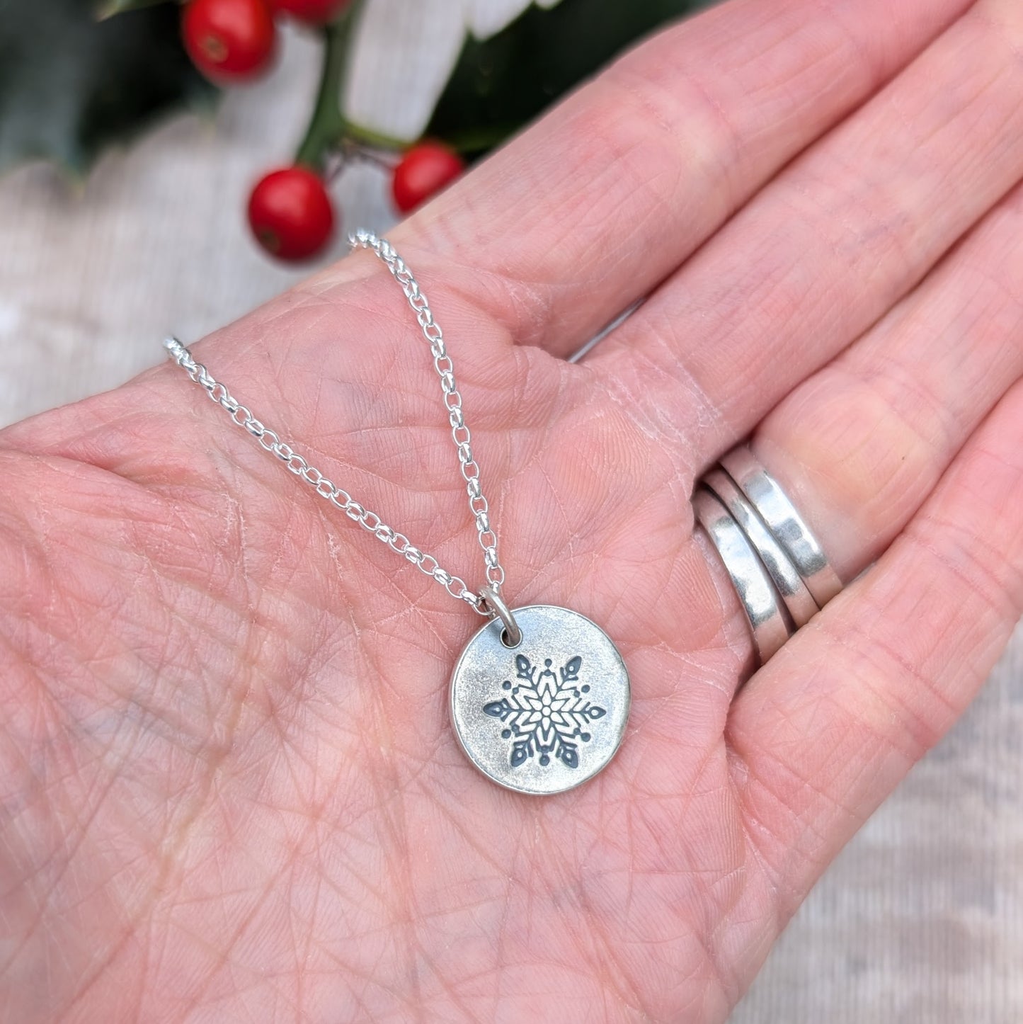 Silver disc pendant necklace featuring a single engraved snowflake design hand stamped onto the disc. Suspended from an 18 inch silver chain via a small open circle link.