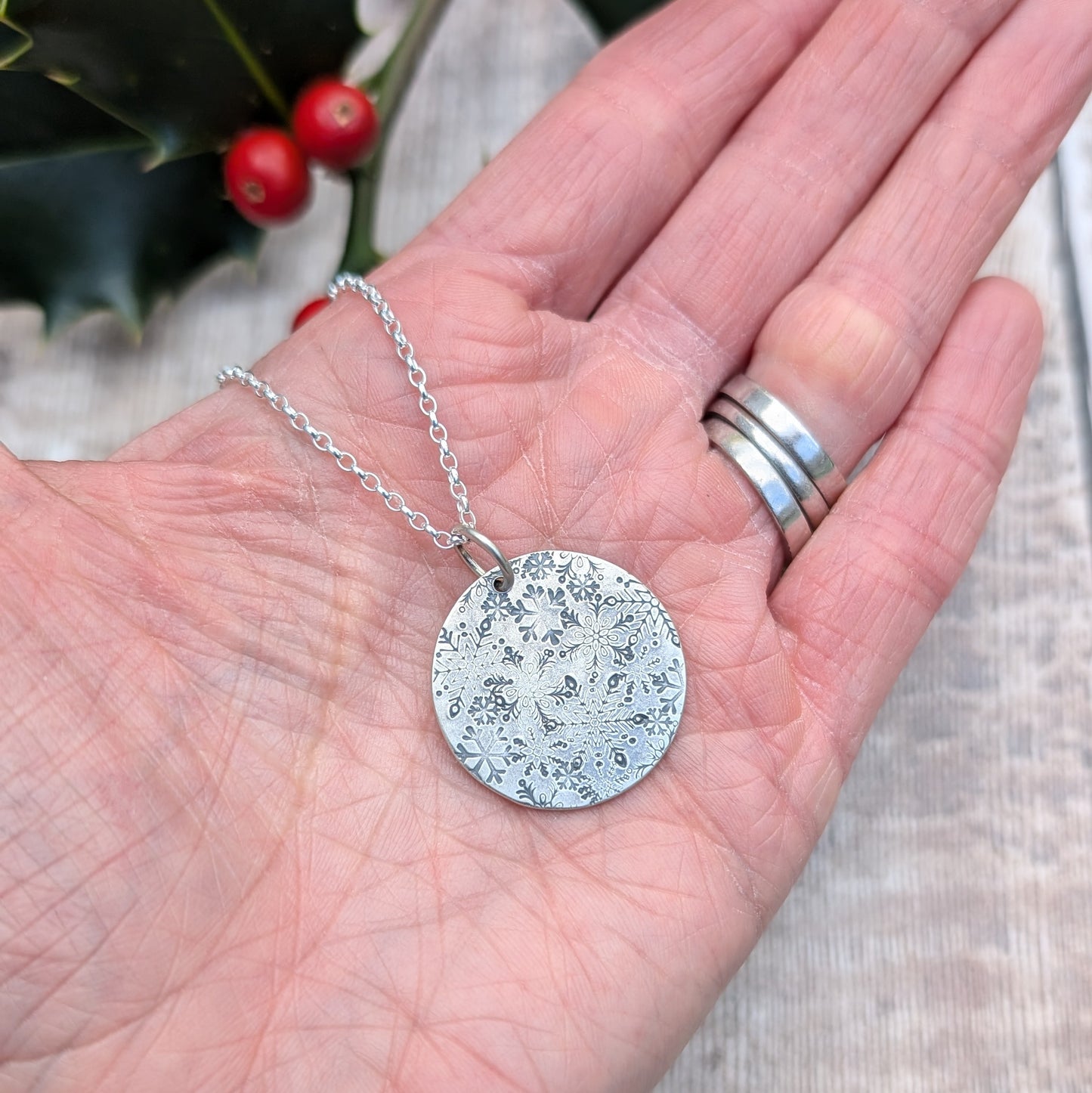 Pendant is a silver disc with intricate stamped snowflakes, some raised and some indented in texture. The snowflakes are randomly stamped and are all different in size and shape. Suspended from an 18 inch silver chain via a small open circle link.