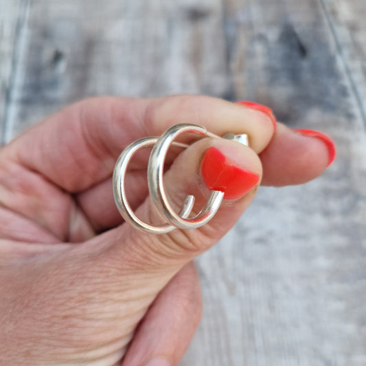 A hand holding a pair of sterling silver oval wire hoop earrings, showcasing their smooth, polished finish.