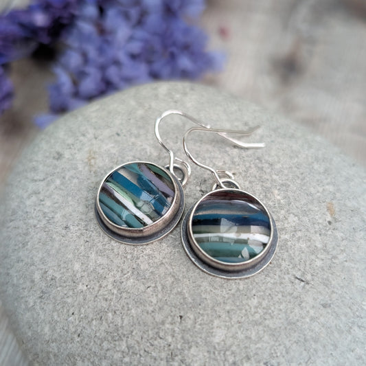 Each earring is a round surfite stone set in an oxidised silver bezel, suspended from silver earring wire. Surfite has random horizontal uneven stripes of lilac, blue, turquoise, green, white and black, gloss finish.