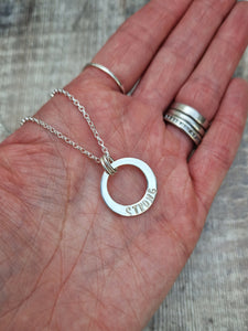 Sterling Silver ‘STRONG’ necklace. Silver disc with offset hole in centre, looks like a thick circle. Attached via two small silver hoops to silver chain. On thicker part of disc, inscription wording hammered into the silver reads STRONG in capitals. Disc measures approximately 20 mm in diameter. Chain length 16, 18 or 20 inches.