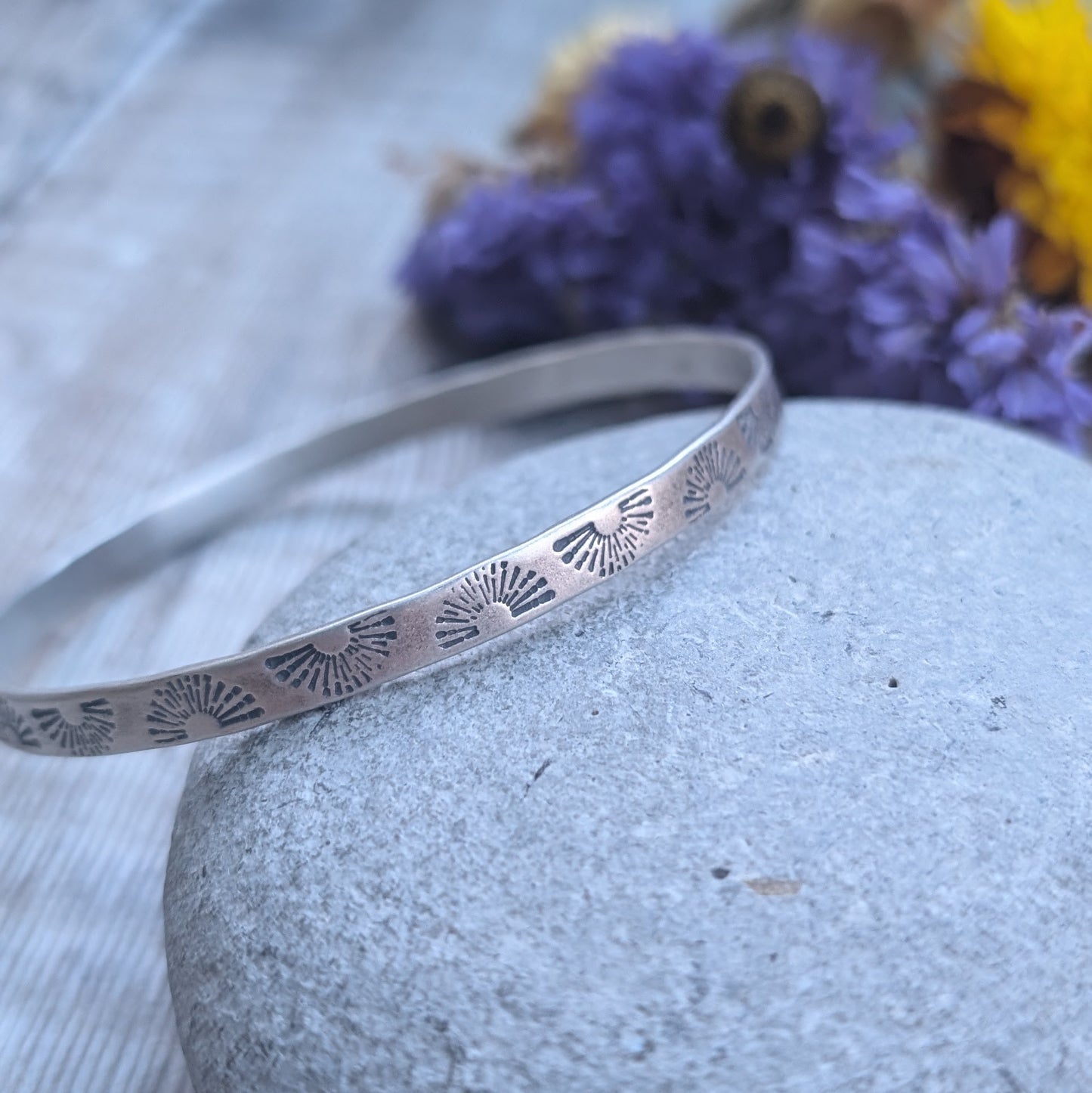 Sterling Silver bangle stamped with repeating sunburst pattern.