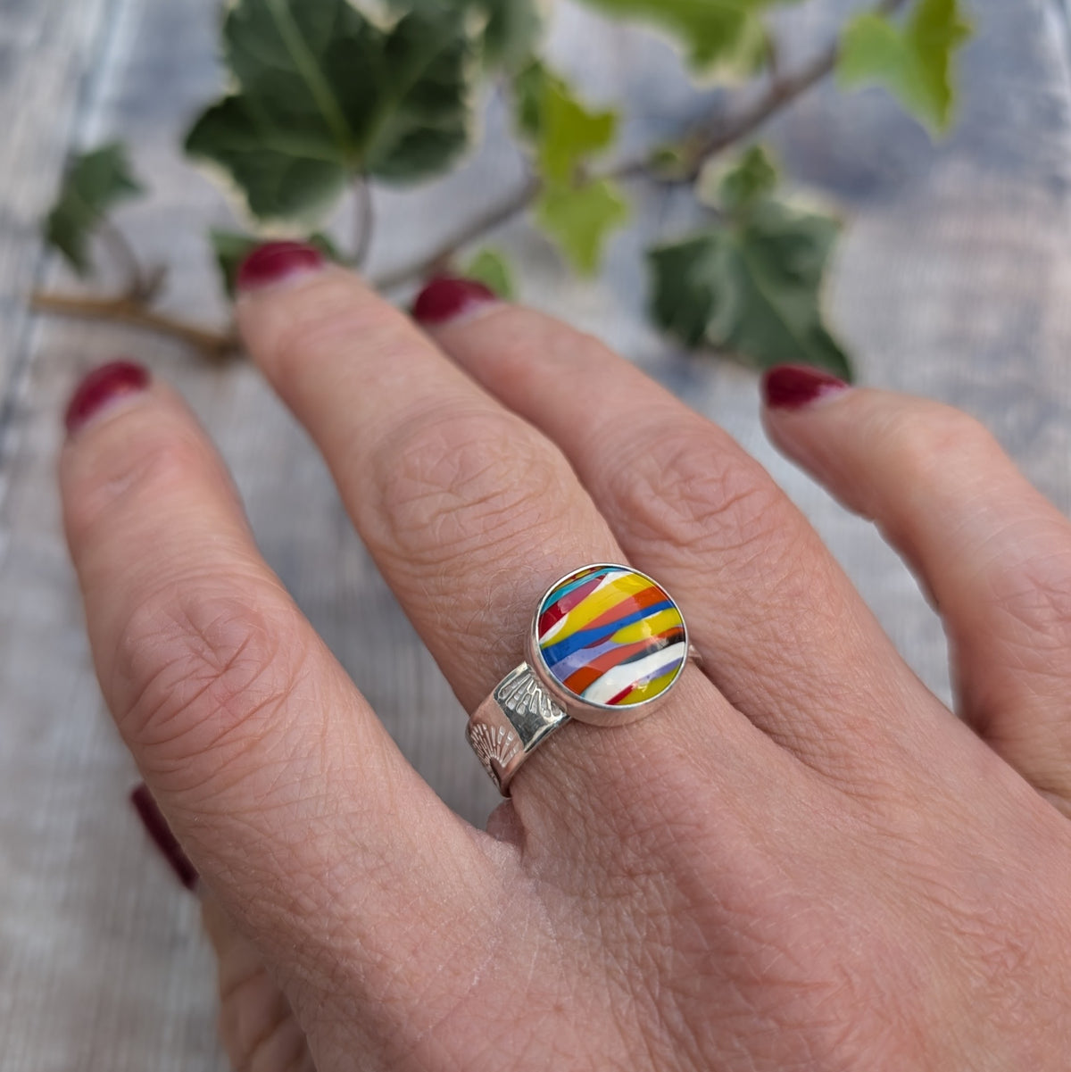 Silver sunrise surfite ring worn on a finger, showing the bright multicoloured Surfite stone and hand stamped sunrise pattern on the silver band.