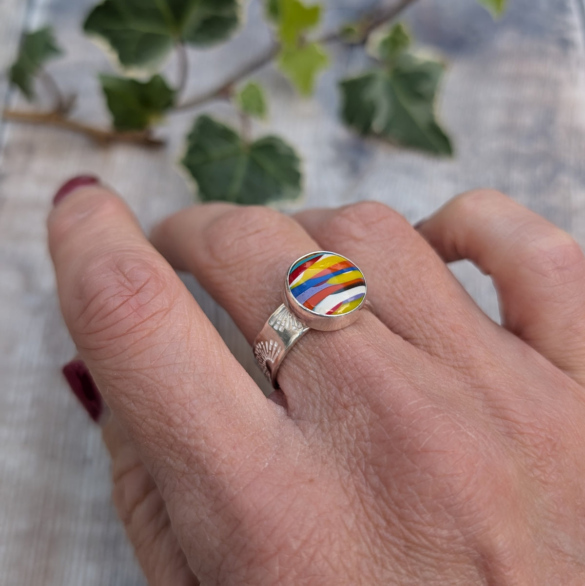 Close up of silver sunrise surfite ring being worn, featuring a round Surfite stone with colourful stripes of yellow, blue, red, orange and white.