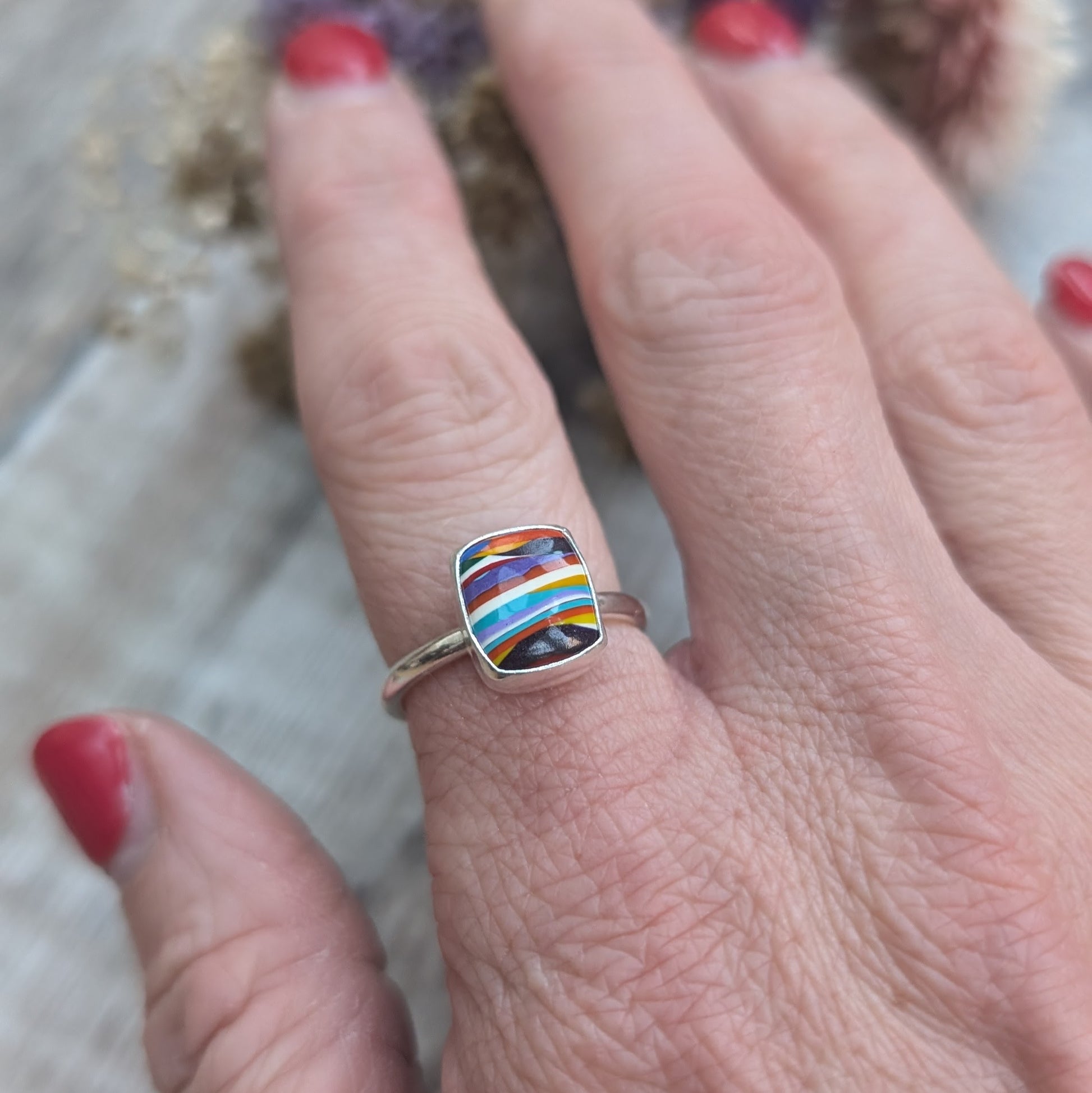 Sterling Silver rectangular shaped surfite ring. Resin stone with rounded edges and gloss surface measuring approximately 10 x 8 mm. Set in a silver bezel and mounted on silver ring band approximately 2 mm wide. Uneven horizonal stripes of colour are mainly orange, blue, black, white, red and yellow.