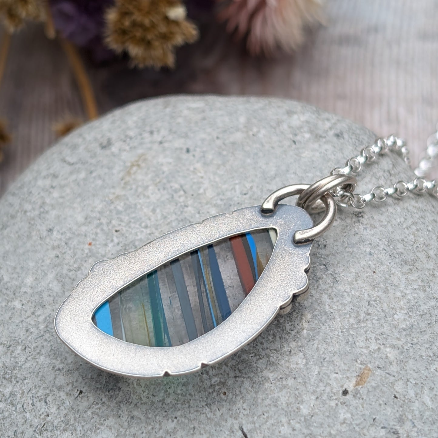 Close-up of the back of a Surfite necklace featuring a teardrop-shaped recycled Surfite stone with colourful stripes, set in an oxidised sterling silver frame with a smooth finish.