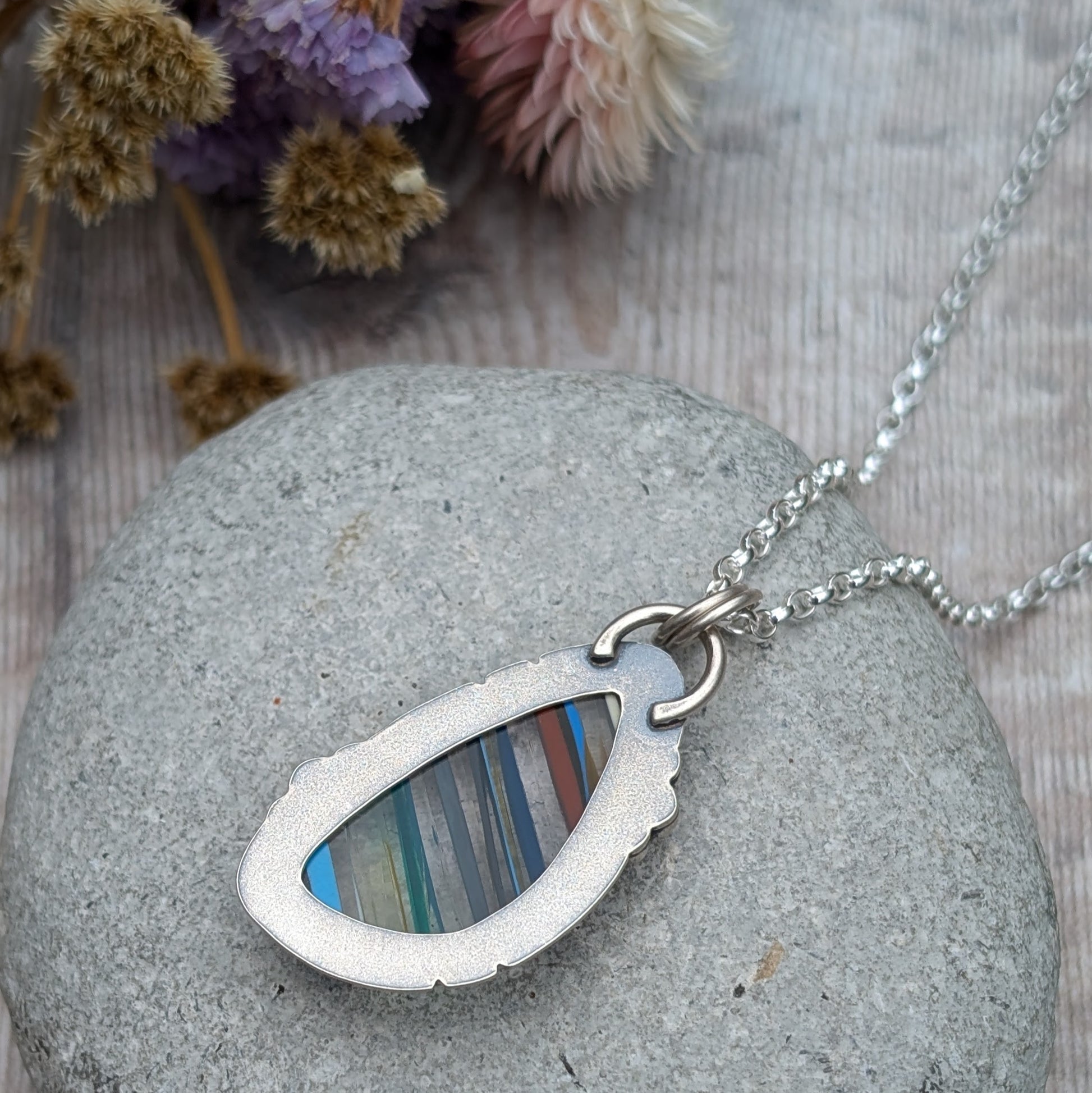 Close-up of the back of a Surfite necklace featuring a teardrop-shaped recycled Surfite stone with colourful stripes, set in an oxidised sterling silver frame with a smooth finish.