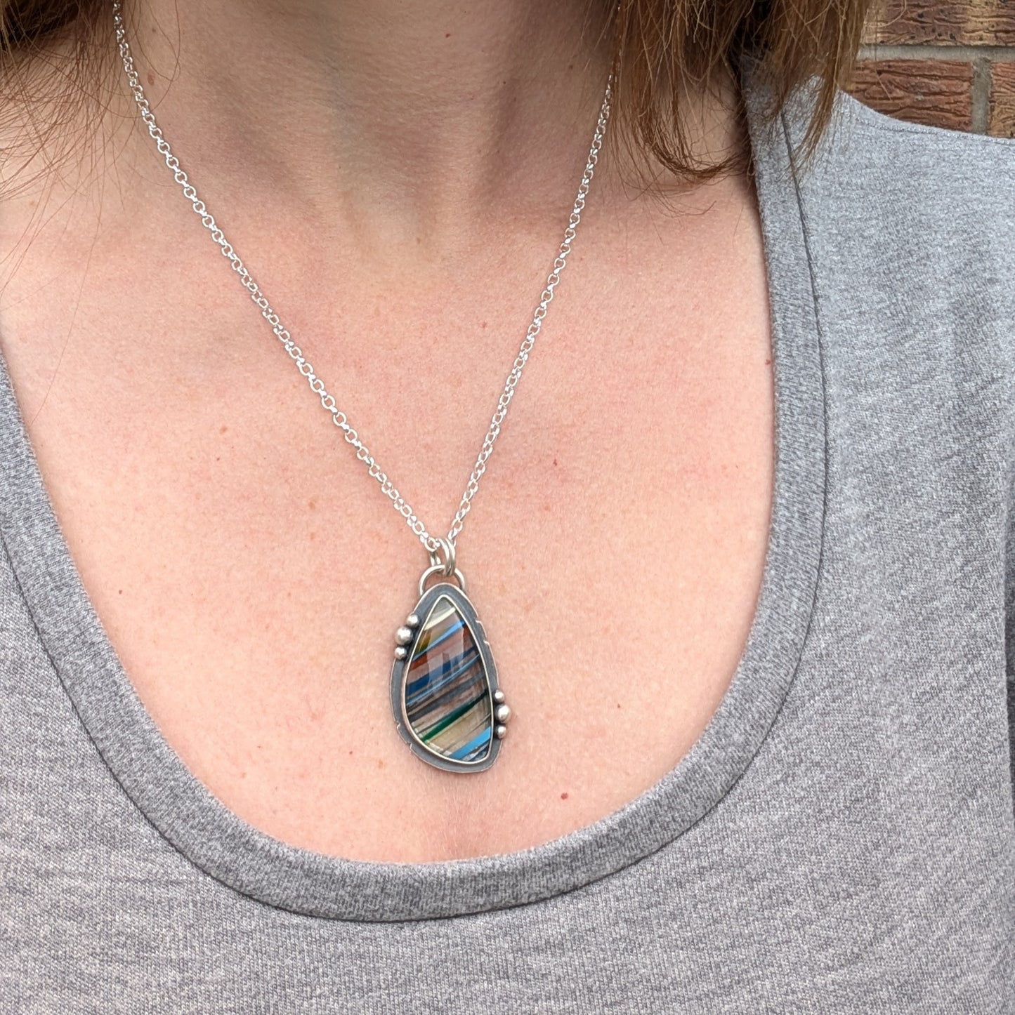 Model wearing the Surfite necklace, showcasing the teardrop-shaped pendant with bold, colourful stripes, hanging from an oxidised silver chain.