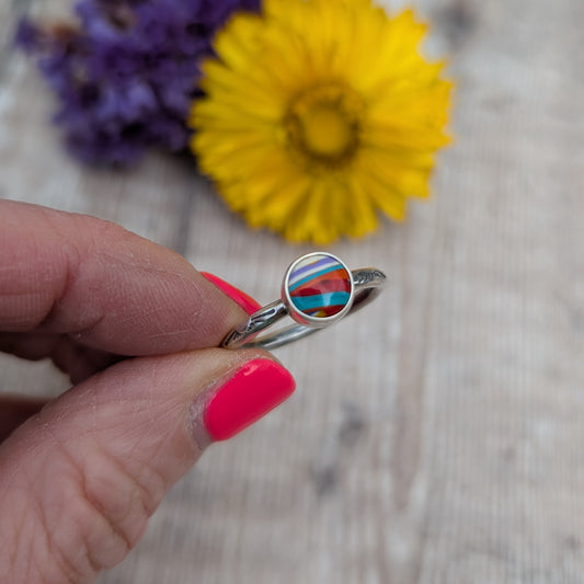 Surfite Ring with Sunburst Stamp held between fingers, showing the colourful Surfite stone and sunburst stamped recycled sterling silver band.